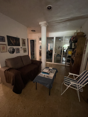 A cozy living room featuring a brown sofa, striped chair, small covered table with books, wall art, bookshelf, pillar, and glass doors leading to another room.