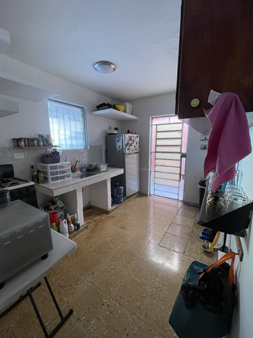 This image shows a small, tidy kitchen with a fridge, sink, stove, shelves, and various items organized on counters and shelves. Light enters from a door.