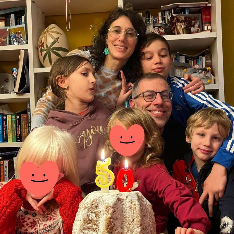 Une famille heureuse se rassemble autour d'un gâteau décoré de 50 bougies pour fêter un anniversaire. Des étagères remplies de livres et des décorations sont visibles à l'arrière-plan. Les visages de deux enfants sont cachés.