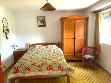 Dieses gemütliche Schlafzimmer verfügt über ein Doppelbett mit einer bunten Patchwork-Decke, einen Kleiderschrank aus Holz, einen Korbstuhl, einen Nachttisch, einen Traumfänger, gerahmte Bilder und ein Fenster mit Vorhang.