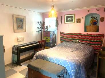 Dieses gemütliche Schlafzimmer verfügt über ein Doppelbett, eine farbenfrohe Einrichtung, ein gemustertes Kopfteil, ein Digitalpiano, einen Holzstuhl, Bilder an den Wänden und eine Mischung aus eklektischen Möbeln.