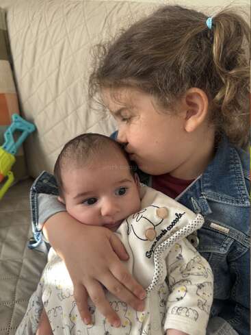 Ein junges Mädchen kuschelt liebevoll mit einem Baby und küsst es, während beide auf einem Sofa sitzen. Der Moment strahlt Wärme, Zärtlichkeit und Geschwisterliebe aus, umgeben von sanfter Geborgenheit.