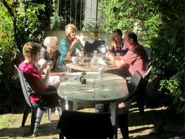 La imagen representa a un grupo de cinco personas reunidas alrededor de una mesa en un jardín, disfrutando de una comida o socializando.