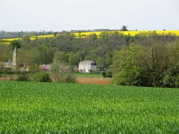 La imagen representa un sereno paisaje rural con una casa blanca, el campanario de una iglesia y un vibrante campo verde en primer plano.