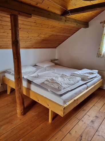 Esse quarto aconchegante no sótão apresenta um teto de madeira, vigas expostas e uma cama de madeira resistente. Um tronco de árvore rústico sustenta o teto, acrescentando charme e personalidade.