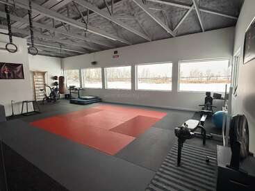 Esta é uma moderna academia de artes marciais ou de ginástica com tapetes vermelhos, anéis de ginástica, equipamentos de exercício, janelas grandes, luz natural brilhante e um design de teto industrial.