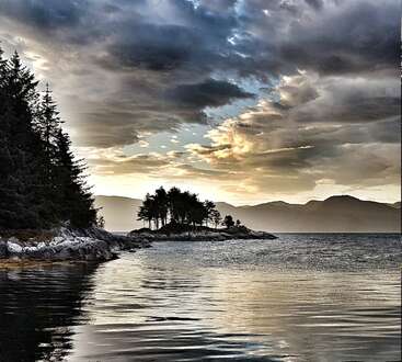 The image depicts a serene lake scene with a small island featuring trees, surrounded by mountains and a cloudy sky, evoking a sense of natural beauty and tranquility.