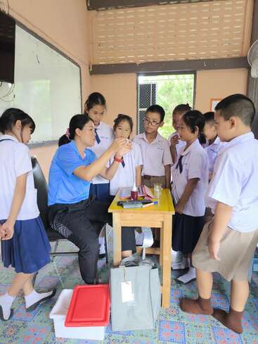 A teacher demonstrates a science experiment to a group of attentive elementary students in a classroom, fostering curiosity and engagement in a hands-on learning environment.