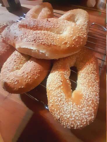 Varios panes recién horneados, dorados y cubiertos de semillas de sésamo, reposan sobre una rejilla para enfriar. Las barras tienen una forma ovalada única y parecen deliciosas.