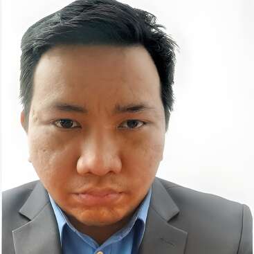 A man with short black hair is wearing a gray suit and blue shirt, looking directly at the camera with a serious and neutral facial expression.
