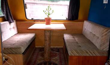 The image shows a cozy interior of a vehicle, featuring a table and chairs, with a window and a door visible, suggesting a comfortable and functional living space.