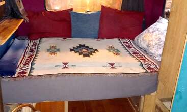The image depicts a cozy room with a bed, showcasing a small, rectangular table and a large, rectangular bed, surrounded by a wooden floor and a white wall, evoking a sense of warmth and comfort.