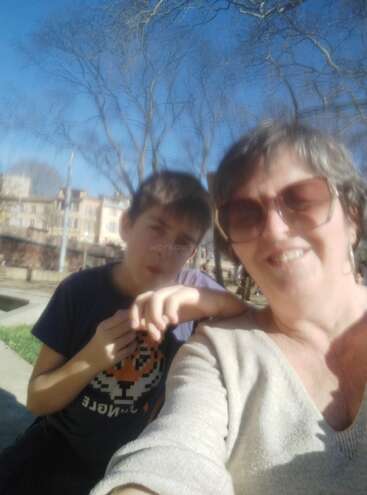 Eine Frau und ein Junge machen an einem sonnigen Tag draußen ein unscharfes Selfie. Im Hintergrund sieht man kahle Bäume und Gebäude. Beide wirken glücklich und entspannt.