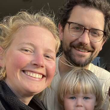 A imagem retrata uma família de quatro pessoas posando para uma foto, com dois adultos e duas crianças, mostrando seu relacionamento caloroso e amoroso. O traje da família é casual e confortável.