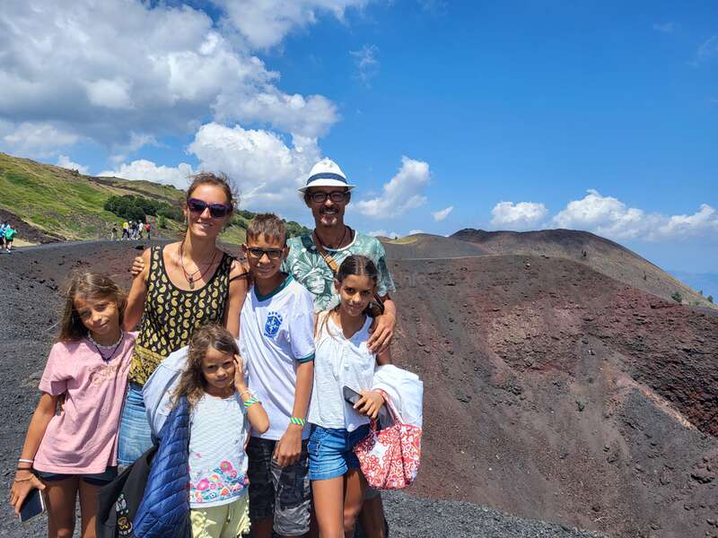La imagen muestra a una familia de seis miembros posando para una foto en una ladera escarpada y rocosa bajo un cielo azul con nubes blancas.
