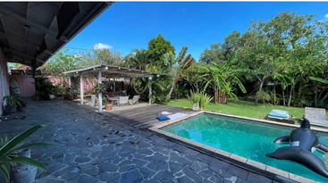 A imagem retrata um ambiente externo sereno, com uma piscina e uma área de pátio ao redor, com uma casa grande ao fundo, evocando uma sensação de relaxamento e tranquilidade.