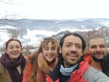 L'image représente trois personnes posant pour un selfie devant un paysage enneigé, les deux femmes se trouvant de part et d'autre de l'homme et portant toutes des écharpes et des vêtements d'hiver.