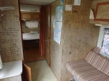 This image shows the inside of a camper or RV, with handwritten notes and maps covering the wooden walls, a bed in the back, and striped seating.