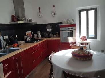 This cozy kitchen features red cabinets, a round table with a woven basket centerpiece, modern appliances, wall decorations, kitchen essentials, and sunlight streaming through a window.