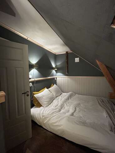 This cozy attic bedroom features a slanted ceiling, soft lighting, white bedding, yellow accent pillows, wood paneling, and a small bed nestled against the wall.