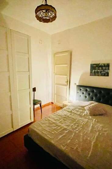 Este acogedor dormitorio cuenta con una cama doble con cabecero empenachado, una mesilla de noche, un armario, una silla individual, iluminación cálida y decoración minimalista.