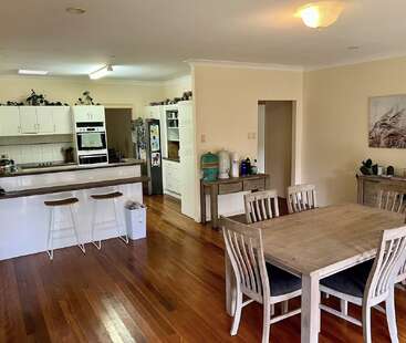 Cette image montre une cuisine et une salle à manger ouvertes et lumineuses, avec des sols en bois, des armoires blanches, une table de salle à manger, des tabourets de bar et des touches décoratives sur les comptoirs.