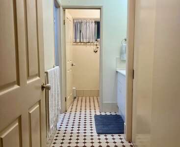 Cette image montre une salle de bains propre et bien éclairée, avec des murs de couleur crème, un carrelage à motifs, des placards blancs, des porte-serviettes et une petite fenêtre avec des rideaux.