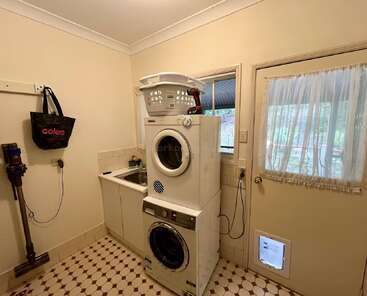 Cette buanderie est équipée d'un lave-linge et d'un sèche-linge superposés, d'un évier, d'un aspirateur fixé au mur, d'un sac à provisions, d'une fenêtre, d'une porte avec chatière et d'un carrelage à motifs.