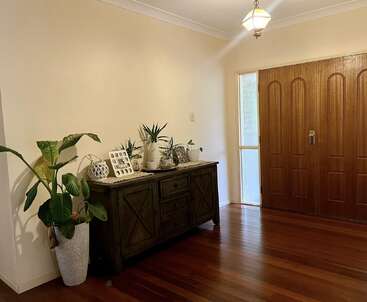 Une entrée confortable avec des planchers en bois, un grand meuble en bois orné de plantes, d'objets de décoration, de photos encadrées et d'une grande plante à côté de doubles portes en bois.