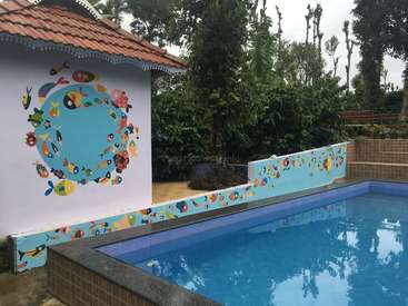 Das Bild zeigt eine ruhige Hinterhofszene mit einem Pool, einem weißen Gebäude mit einer Wandmalerei aus Fischen und üppigem Grün, die ein Gefühl von Ruhe und Entspannung hervorruft.