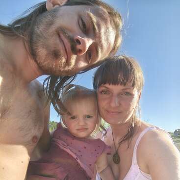 Una selfie familiar al aire libre bajo un cielo azul y despejado. Un hombre, una mujer y un niño pequeño posan muy juntos, sonriendo, irradiando calidez y unión.