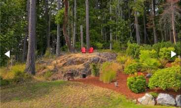 Two bright red chairs sit atop a rocky hill, surrounded by lush green trees and plants, providing a peaceful spot overlooking a beautiful forested landscape.