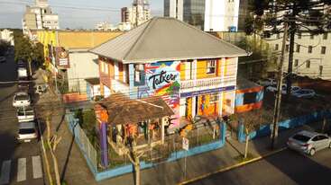 A vibrant, colorful building on a street corner features a large mural reading "Talkers." Surrounded by a blue fence, it stands amidst urban surroundings and parked cars.