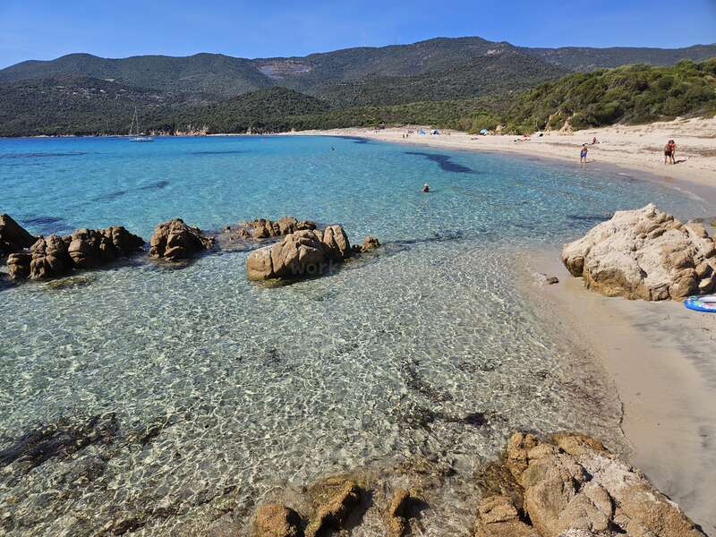 The image depicts a serene beach scene with clear water, large rocks, and a mountainous backdrop, evoking a sense of tranquility and natural beauty.