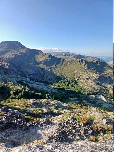 Un paysage montagneux époustouflant avec des terrains rocheux, des vallées verdoyantes et des sommets lointains sous un ciel bleu clair, créant un sentiment de paix et de beauté naturelle.