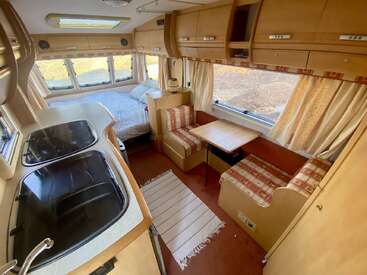 This image shows the cozy interior of a camper van featuring a bed, a small kitchen area with a sink, a dining table, and two benches.