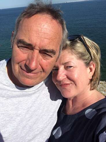 Un hombre y una mujer sonrientes se hacen un selfie en primer plano al aire libre junto al mar en un día soleado, disfrutando de su tiempo juntos con el agua como telón de fondo.