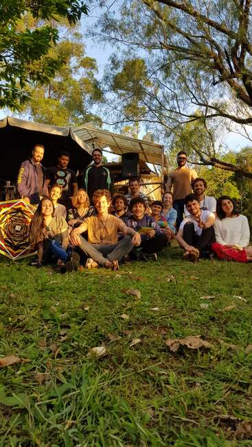Das Bild zeigt eine Gruppe von 15 Personen, die für ein Foto auf der Wiese posieren, mit einem großen Zelt und Bäumen im Hintergrund.