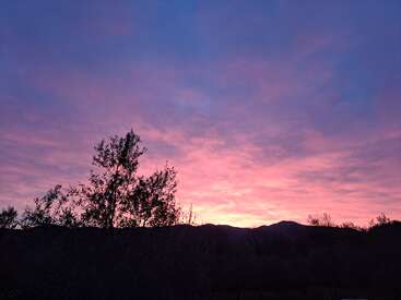 Um lindo pôr do sol ilumina o céu com tons de rosa e roxo. As árvores em silhueta e as montanhas distantes criam uma paisagem tranquila e impressionante ao anoitecer.
