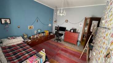 This cozy bedroom features a blue accent wall, single bed, bookshelves, computer desk, red dresser, chandelier, string lights, colorful rug, and butterfly-decorated closet.
