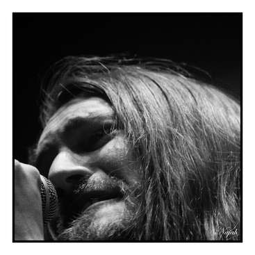 The image is a black-and-white close-up photograph of Kurt Cobain\'s face, with his hair covering his eyes, and a microphone in front of him.