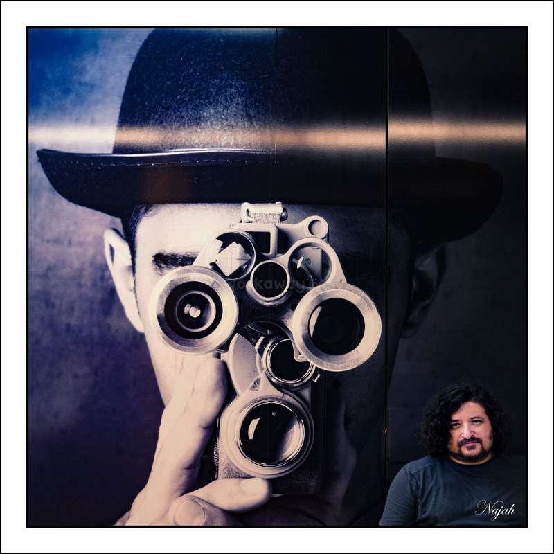 L'image montre un homme tenant un appareil photo ancien à quatre objectifs, coiffé d'un chapeau melon, à côté d'une photo plus petite d'un autre homme aux cheveux et à la barbe foncés.