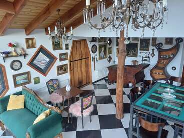 Dieser gemütliche, eklektische Raum ist mit Vintage-Möbeln, karierten Böden, Kronleuchtern, Wandkunst, schrulligen Fenstern, einem grünen Sofa, hölzernen Akzenten und dekorativen Regalen mit einzigartigem Dekor ausgestattet.