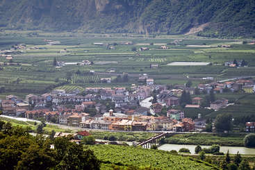 Das Bild zeigt eine ruhige Landschaft mit einem kleinen Dorf und einem Fluss, umgeben von üppigem Grün und Bäumen, die ein Gefühl von Ruhe und natürlicher Schönheit hervorrufen.