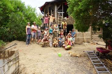 L'image représente un groupe de personnes, enfants et adultes, posant pour une photo devant un bâtiment partiellement construit, entouré d'éléments naturels.