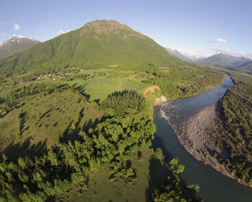 L'image représente un paysage serein avec une rivière coulant dans une vallée luxuriante, entourée de montagnes majestueuses et d'un ciel bleu clair.