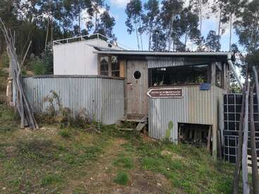 This rustic building, surrounded by greenery and tall trees, features corrugated metal walls, wooden doors, and a sign reading "Centro de Interpretación de la Naturaleza."
