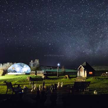 L'image représente un cadre extérieur serein de nuit, avec un dôme géodésique, une petite maison et un échiquier, le tout sur fond de ciel étoilé.