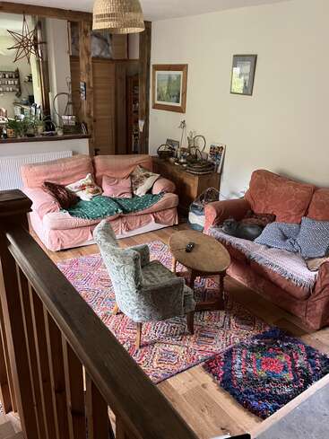 This cozy living room features mismatched sofas, colorful rugs, a wooden coffee table, eclectic decor, framed artwork, houseplants, and warm lighting, creating a welcoming, lived-in atmosphere.