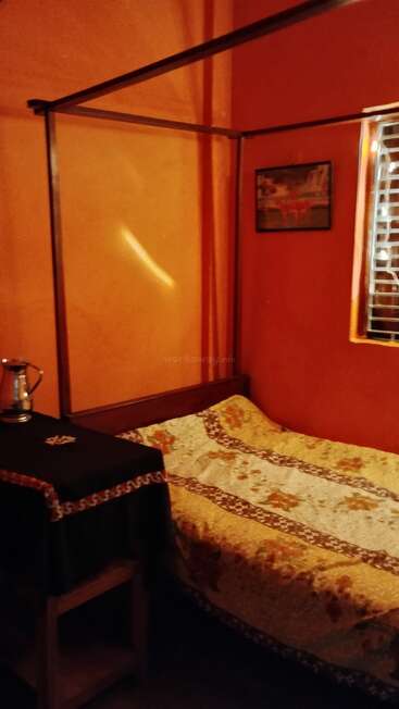 L'image représente une chambre à coucher confortable avec un lit à baldaquin, une fenêtre avec des stores et une table avec une nappe noire et un pichet en argent.